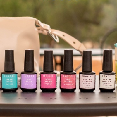Seis frascos de verniz gel com rótulos coloridos e texto INOCOS sobre mesa preta com bolsa bege ao fundo