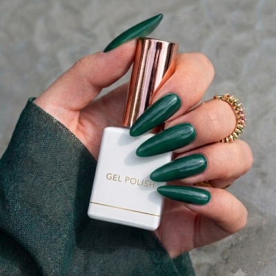 Unhas longas verdes segurando frasco de verniz gel branco e dourado