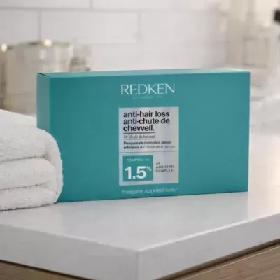 Caixa azul turquesa do produto Redken anti-hair loss com texto em inglês e francês sobre bancada