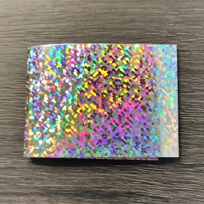 Folha de papel holográfico com padrão de pontos coloridos sobre madeira escura