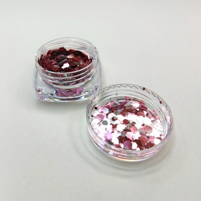 Duas caixas pequenas transparentes com glitter hexagonal rosa, vermelho e branco sobre fundo branco.