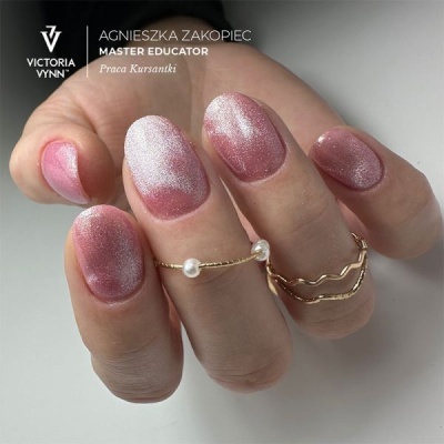 Unhas com verniz rosa e branco cintilante, mão com anéis dourados, fundo cinza claro com texto