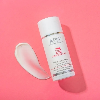 Frasco branco de creme facial APIS sobre fundo rosa com creme aplicado ao lado
