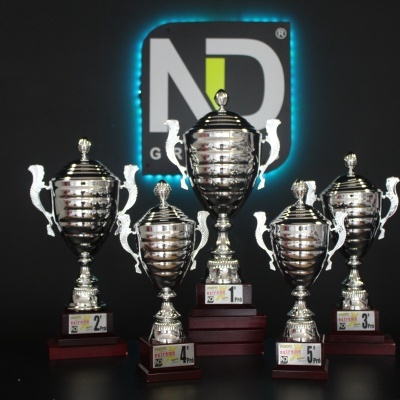 Cinco troféus prateados com etiquetas de posição em base de madeira