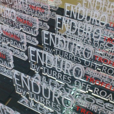 vários troféus transparentes gravados em branco e vermelho numa prateleira