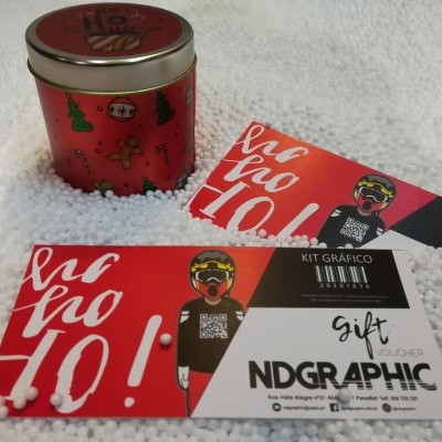 Lata vermelha natalícia com dois cartões gráficos vermelhos e pretos sobre esferas brancas.