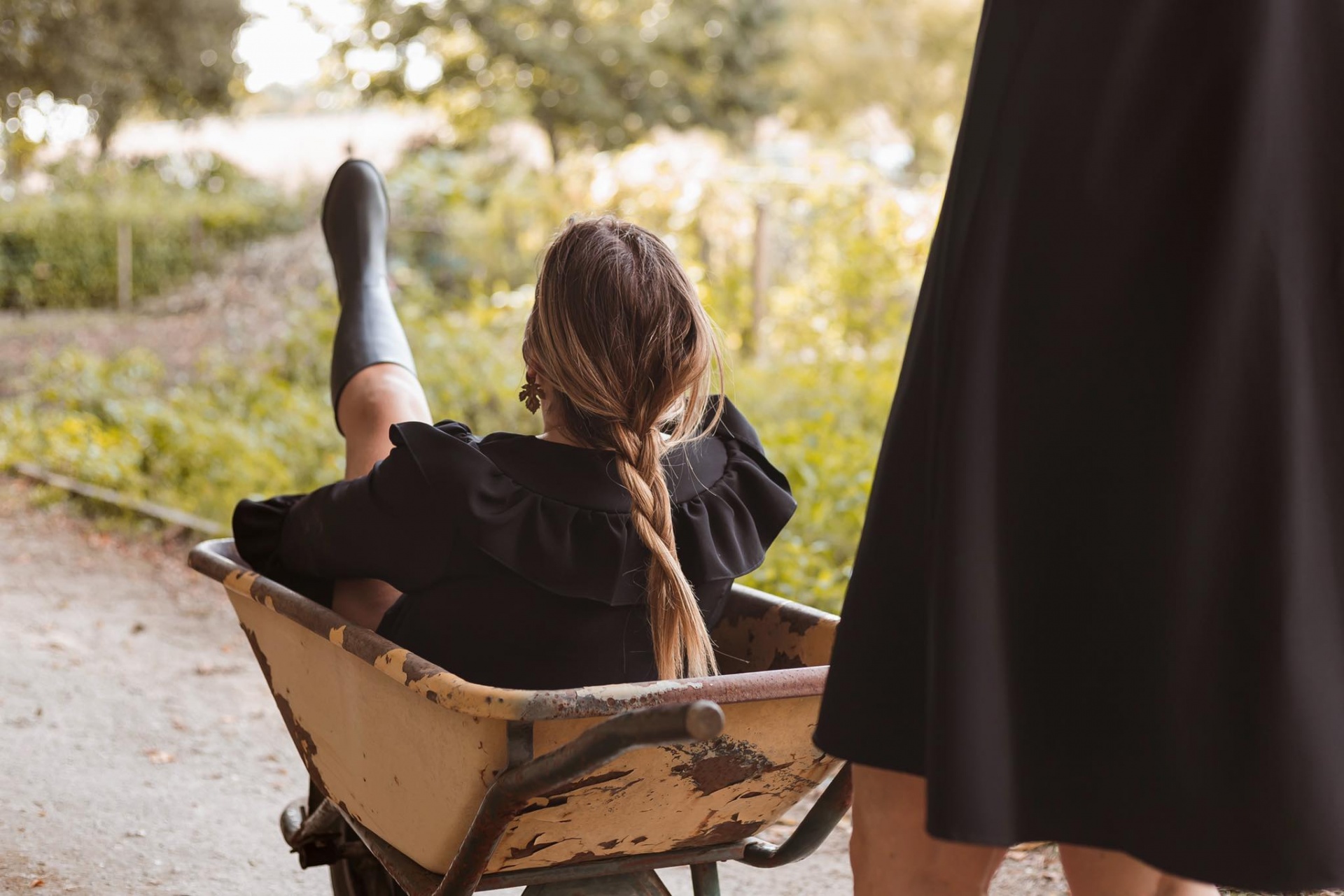 Mulher sentada em carriola de metal envelhecida com vestido e botas pretas ao ar livre