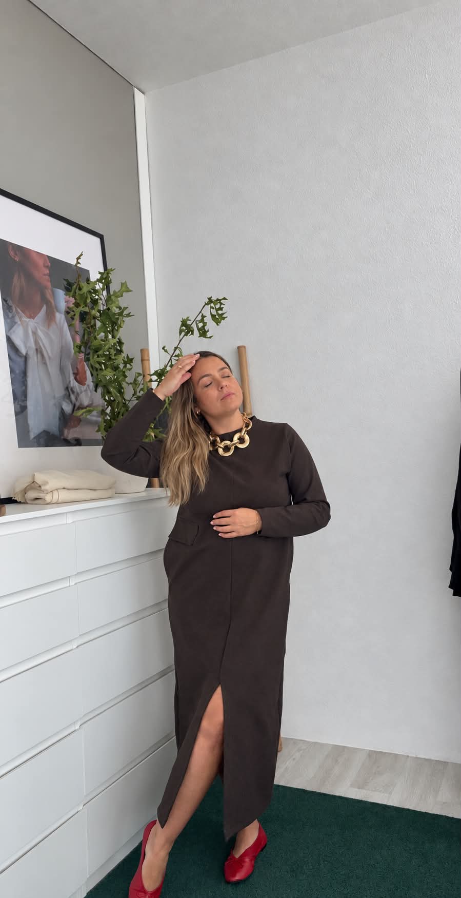 Vestido Antonieta Mulher com vestido castanho escuro e sapatos vermelhos num ambiente interior minimalista