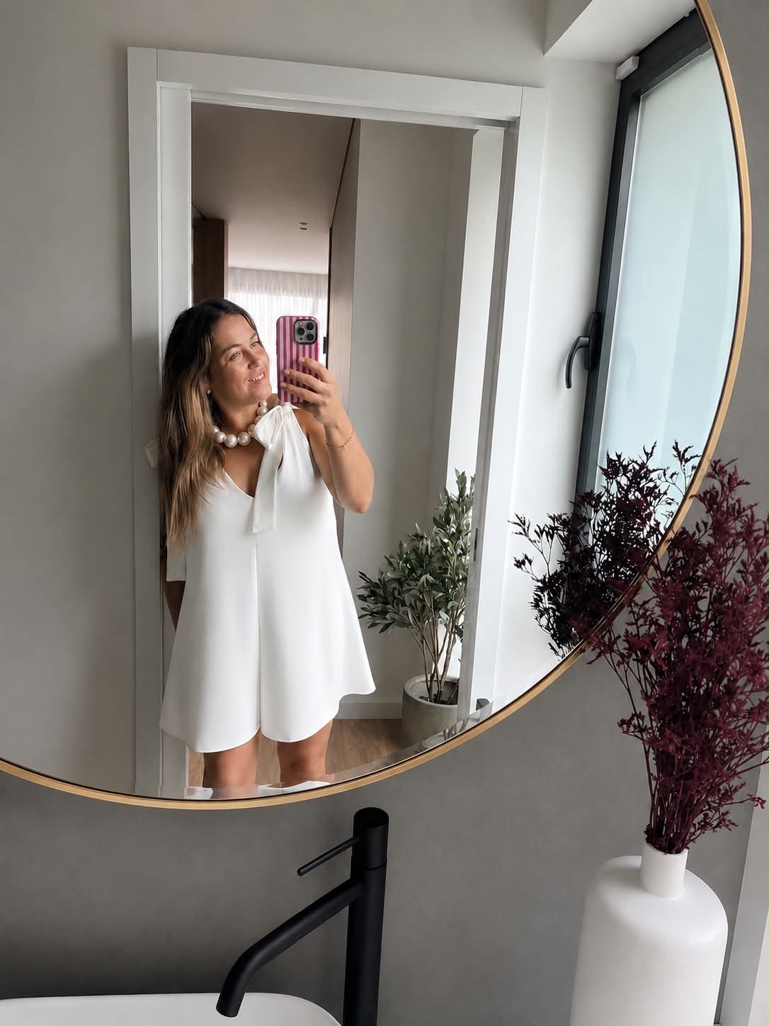 Jumpsuit Formentera Mulher com vestido branco a tirar selfie em espelho redondo num banheiro moderno.