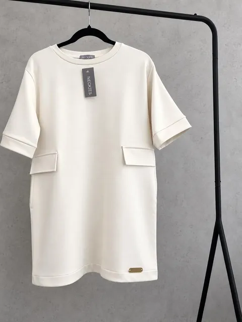Vestido Maddy Vestido branco creme com bolsos, etiqueta NECKTIES e placa metálica pendurado em suporte preto.