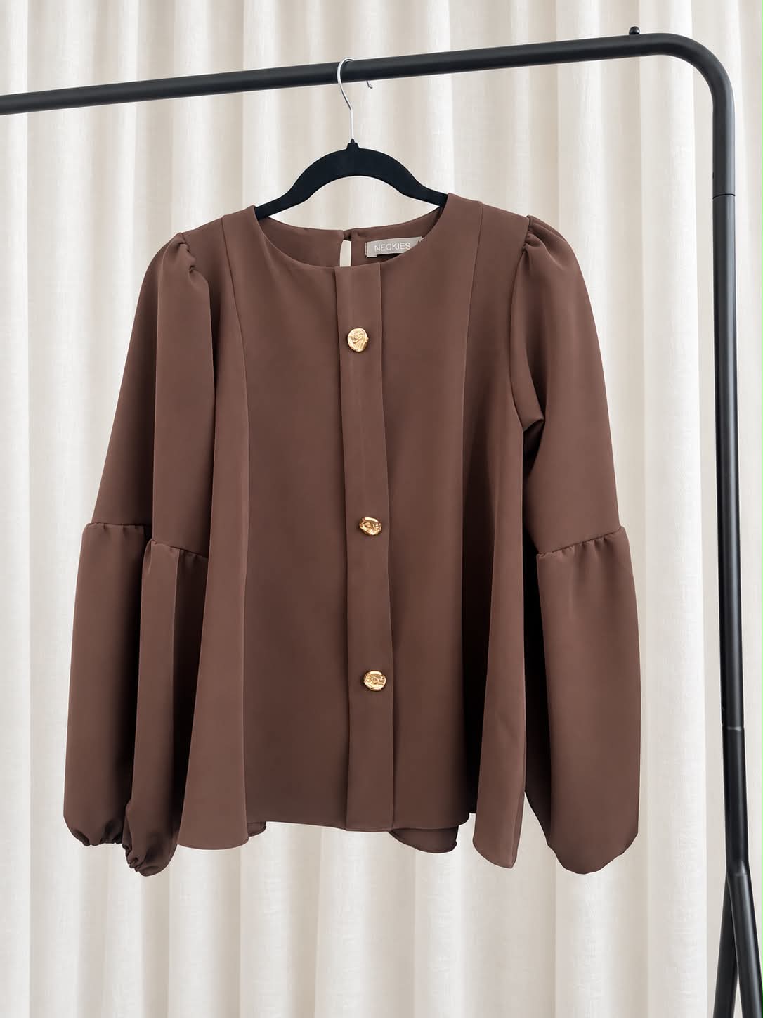 Túnica Isa Blusa castanha com botões dourados pendurada num cabide