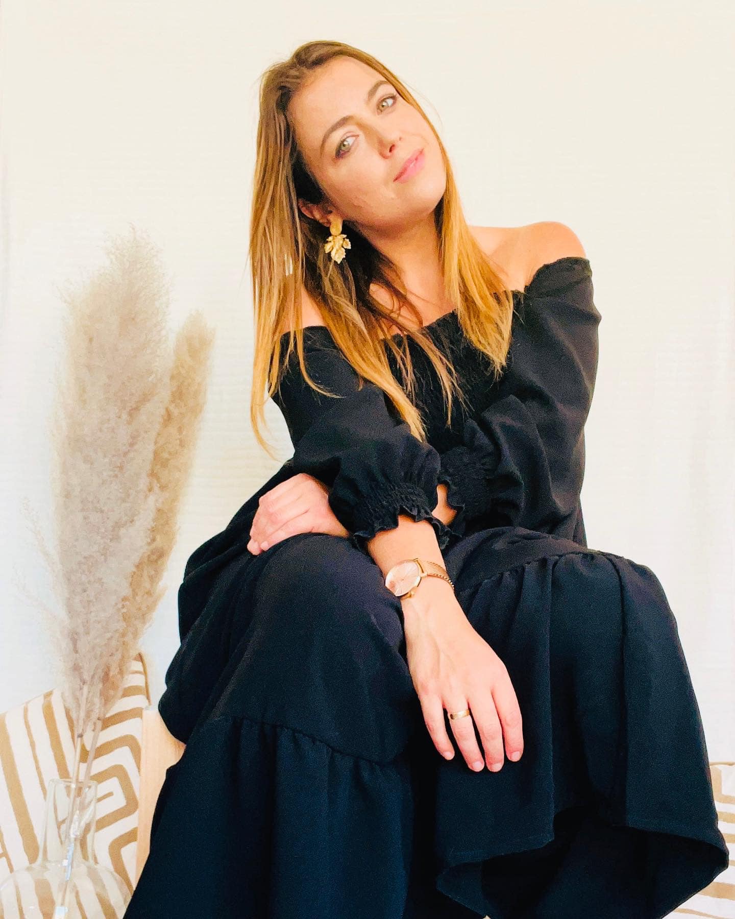 Mulher vestindo vestido preto comprido ombro a ombro com manga comprida e acessórios dourados