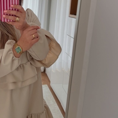 Relógio dourado com mostrador verde e vestido bege com folhos