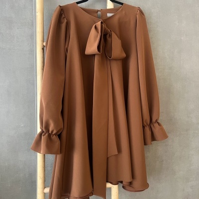 Vestido castanho com laço no decote pendurado em cabide preto