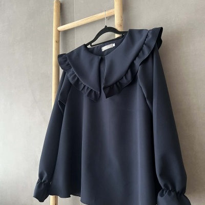 Blusa azul escura com gola ampla e folhos pendurada em suporte de madeira