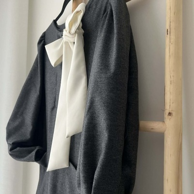 Vestido cinzento com laço branco pendurado numa estrutura de madeira