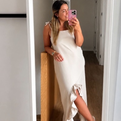 Mulher com vestido longo bege e sandálias, a tirar selfie num espelho dentro de casa