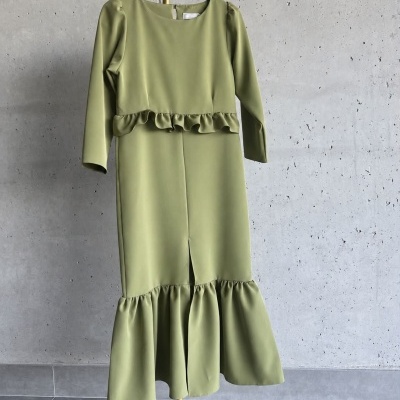 Vestido verde claro com babados pendurado num suporte contra parede cinza