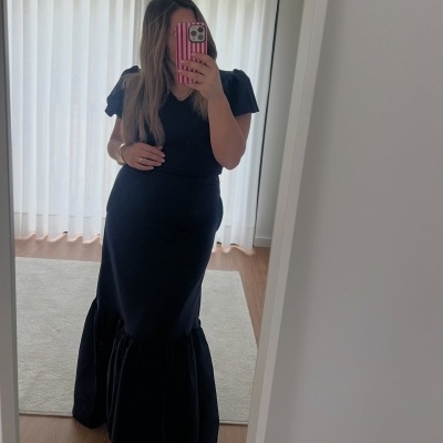 Vestido comprido preto com mangas curtas franzidas e bainha ampla, mulher em frente a espelho