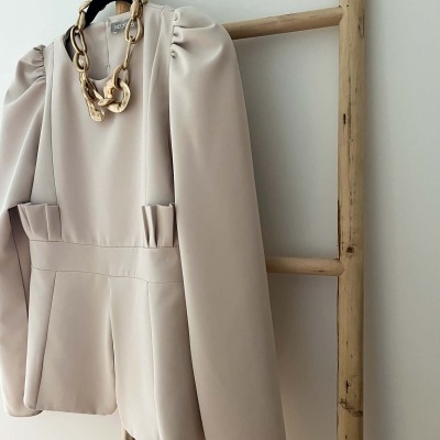 Blazer bege claro com colar dourado pendurado numa escada de madeira