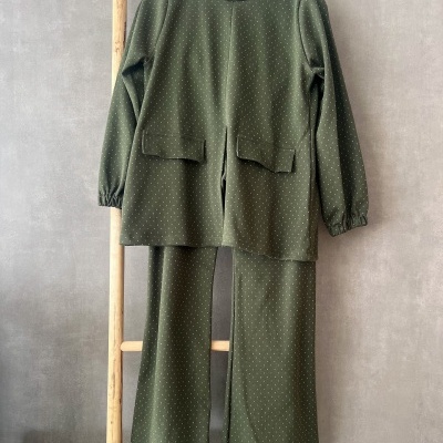 Conjunto verde escuro com pequenos pontos brancos, camisola com bolsos e calças pendurado em estrutura de madeira