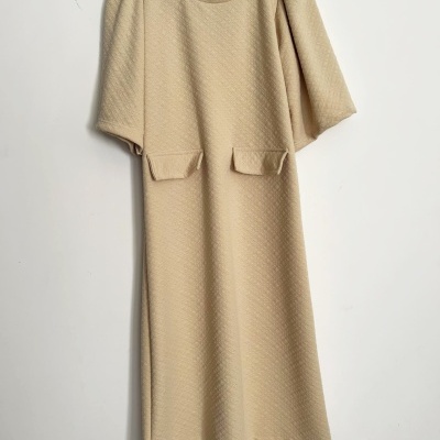 Vestido bege com mangas curtas bufantes e bolsos frontais pendurado num cabide