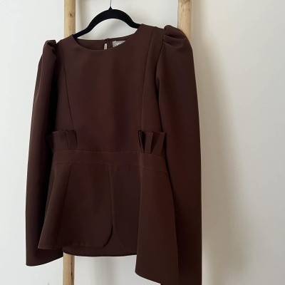 Blusa castanha com mangas compridas em cabide preto numa estrutura de madeira