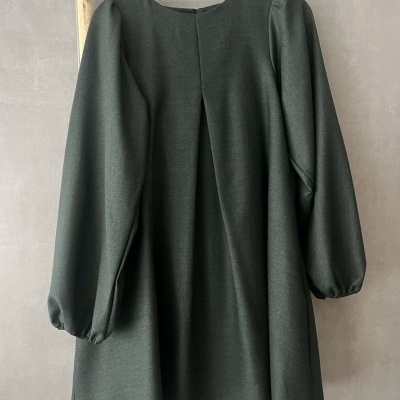 Vestido verde escuro com mangas compridas e prega atrás pendurado num cabide