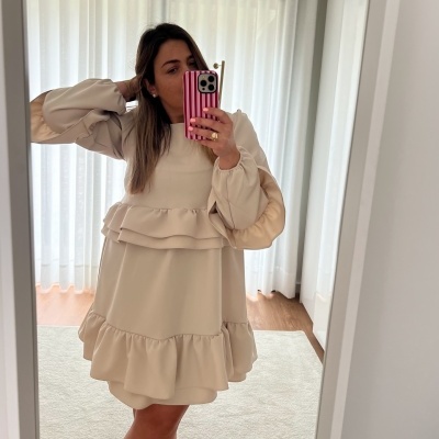 Vestido bege claro com folhos e mangas bufantes num quarto com cortinas brancas.
