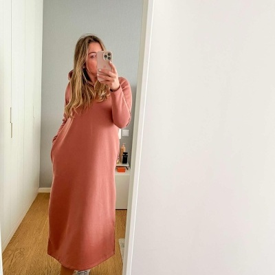 Mulher a tirar selfie com vestido rosa queimado e ténis brancos, espelho num quarto minimalista