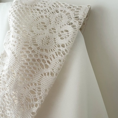 Colar de malha bege com padrão de renda floral sobre superfície branca