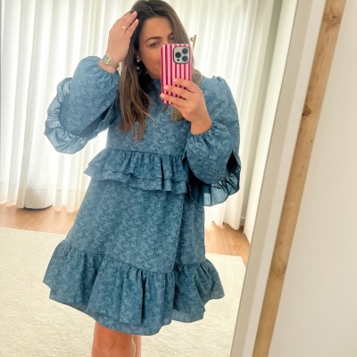 Vestido azul com padrão floral, mangas e saia com folhos, em ambiente interior claro