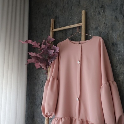 Vestido rosa claro com botões grandes e mangas bufantes pendurado em suporte de madeira