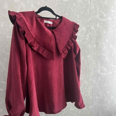 Blusa vermelha de tecido aveludado com gola de babados pendurada num cabide