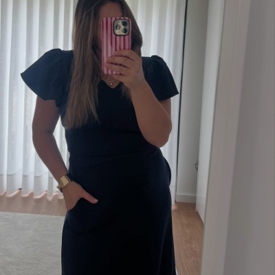 Mulher de vestido preto com mangas bufantes e telemóvel com capa às riscas vermelhas e brancas