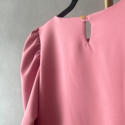 Blusa rosa com manga franzida e botão dourado pendurada em cabide