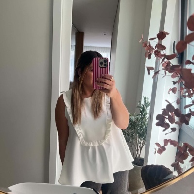 Blusa branca com folhos vista no espelho, planta ao lado da janela e smartphone listrado