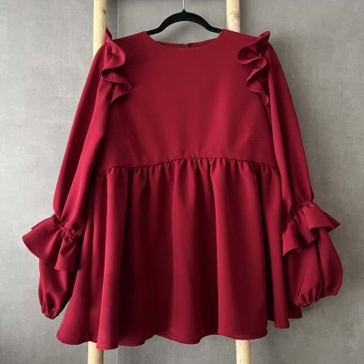 Blusa vermelha com folhos nos ombros e punhos, pendurada em escada de madeira