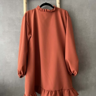 Vestido comprido ferrugem com folhos à gola e bainha pendurado em cabide.