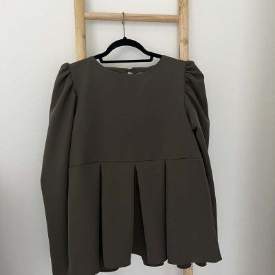 Blusa cinza escuro com mangas franzidas pendurada numa escada de madeira