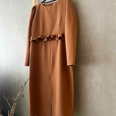 Vestido castanho com mangas compridas pendurado numa escada de madeira.