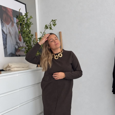Mulher com vestido castanho escuro e sapatos vermelhos num ambiente interior minimalista
