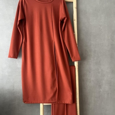 Conjunto de roupa terra pendurado em cabide numa escada de madeira clara junto a parede cinza