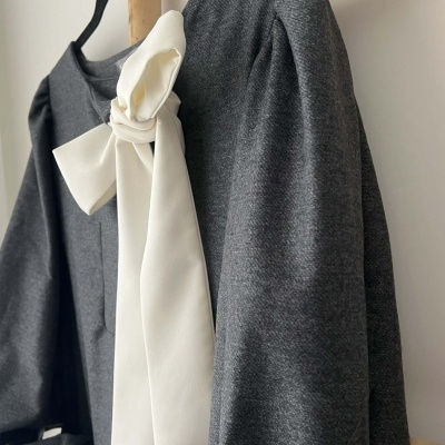 Blusa cinzenta com laço branco pendurada num cabide preto