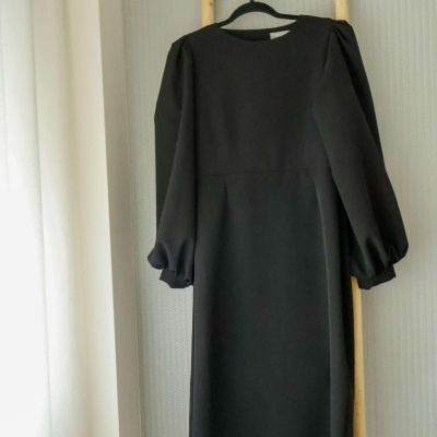 Vestido midi preto com mangas compridas pendurado numa escada de madeira clara