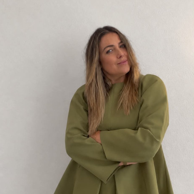 Mulher com blusa verde oliva e calças brancas sobre fundo branco