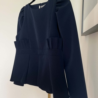 Blusa azul-marinho de manga longa com detalhes franzidos pendurada em cabide