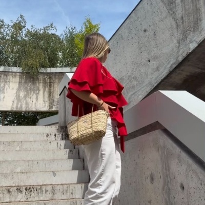 Mulher com blusa vermelha, calças brancas largas e bolsa de palha em escadas urbanas