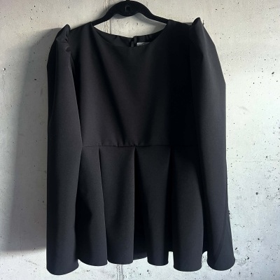 Blusa preta de manga longa com folhos, pendurada numa parede de concreto cinza