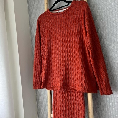 Conjunto de pijama vermelho alaranjado em malha texturizada pendurado numa estrutura de madeira